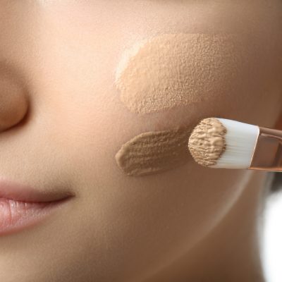 Girl applying foundation and concealer with brush on white background, closeup. Face contouring